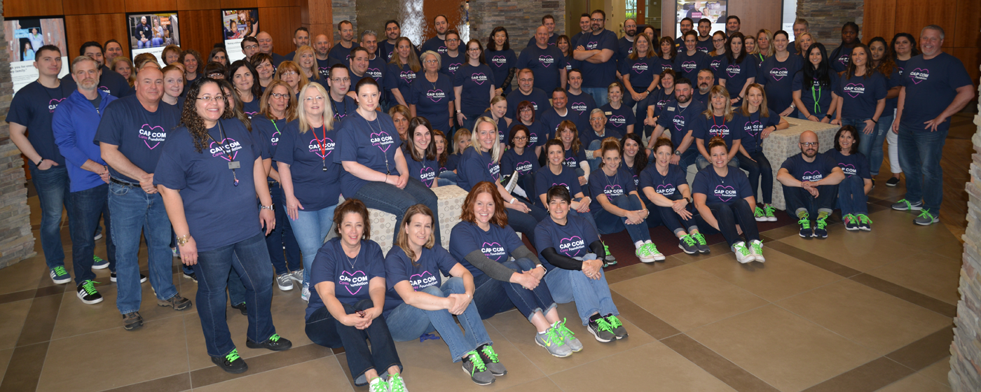 A large group of CAP COM employees wearing their CAP COM Cares Foundation shirts