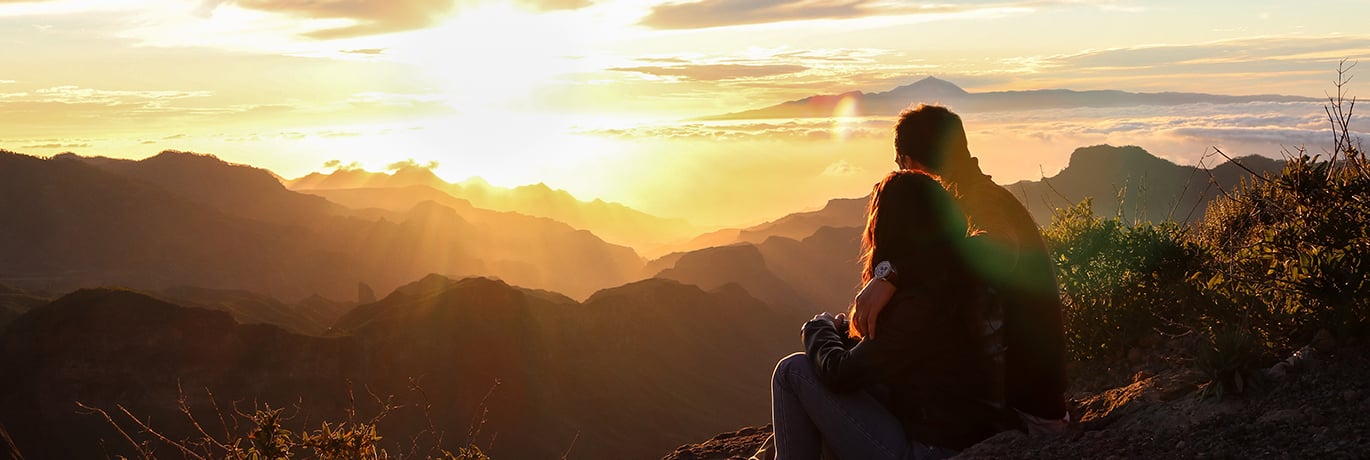 Couple sitting on a mountain watching the sunset