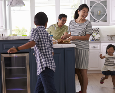 An Asian family in their kitchen with their children running around