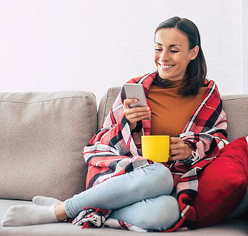 Woman comfy on her couch looking at her phone