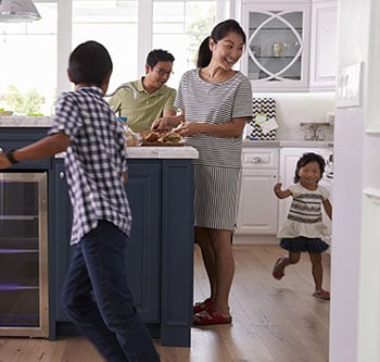 Two kids running around kitchen while their parents cook