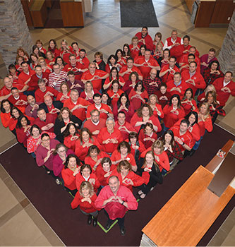 Group of CAP COM employees wearing red or pink t-shirts and standing in the shape of a heart