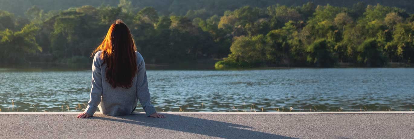A woman sitting looking at a lake on a sunny day.