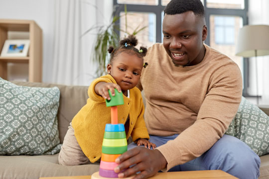 A black man sitting on a couch playing with his baby daughter.