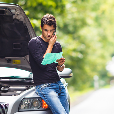 Man leaning on his car while on the phone and looking at paper