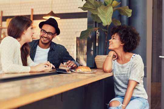 Three friends sitting at a counter sharing food.