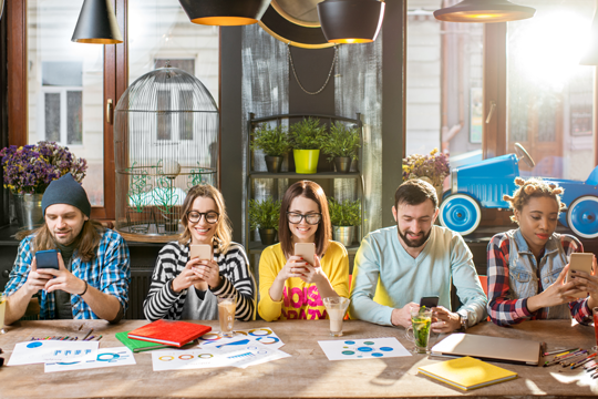 Group of five friends looking through their phones together