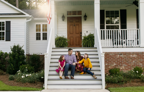 A family sitting on the front stairs of their house.