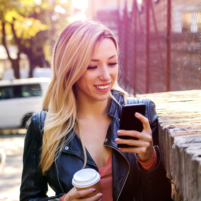 Woman looking at phone and holding cup of coffee