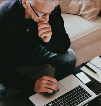 An older man sitting on his couch doing work on his laptop