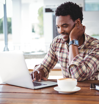 A young black man sitting at the kitchen table with coffee and his laptop