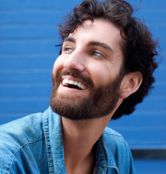 A man with a beard looking off into the distance smiling.