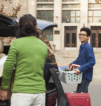 An Asian student unpacking a car with his mom in front of his college dorm.