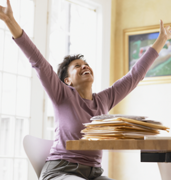 A black woman sitting at her table rejoicing with her arms in the air