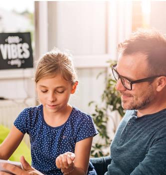 A father and daughter sitting at the kitchen table looking at a tablet