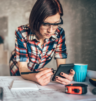 A woman contractor looking at her smartphone over building plans