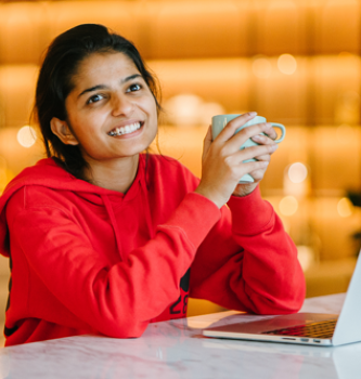 An Indian woman holding a mug while working on her laptop.